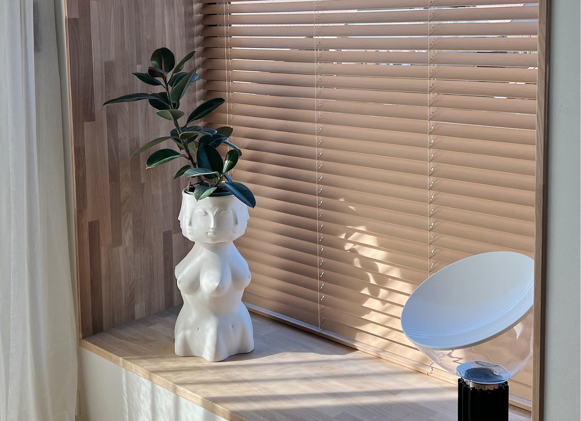 Tre-persienner, 50 mm Vindusnisje med trepersienner, vase med plante og lampe. Foto.